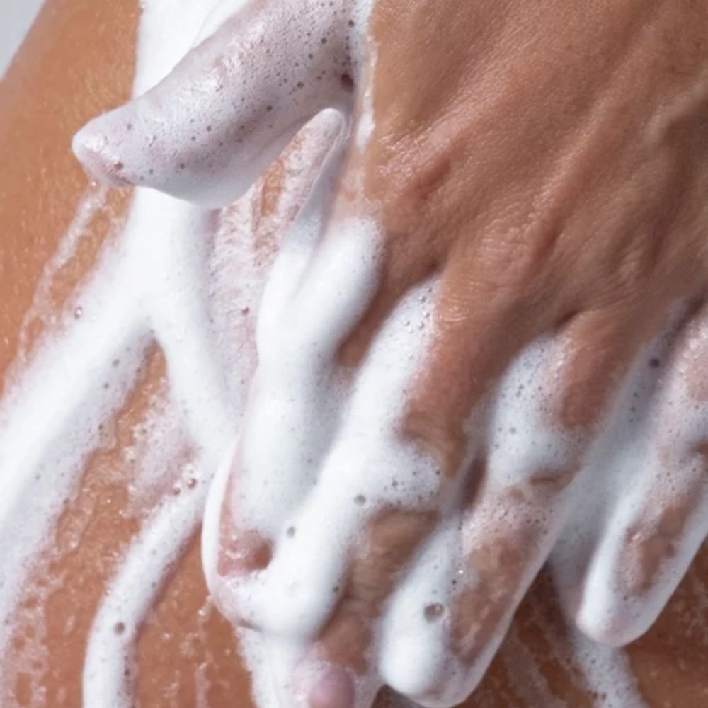 Close-up of a hand lathering soap or body wash with thick white foam on skin.