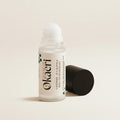A clear cylindrical bottle with a white rollerball top and a black cap, shown on a clean white background. The bottle has a white label with dense black text, and the black cap is placed beside it.