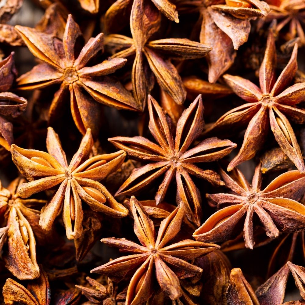 A close-up pile of whole star anise spices, showing their characteristic eight-pointed brown star shape with warm golden-brown highlights.
